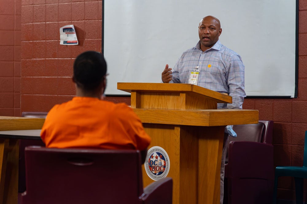 Tyrone Walker speaks from a podium as a Georgetown Prison Scholar listens.