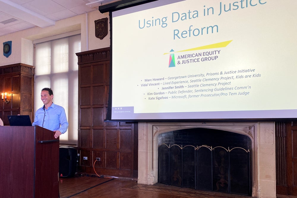Marc Howard smiles at a podium in front of a screen that reads: Using Data in Justice Reform.
