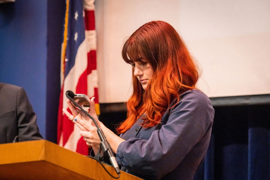 A young woman holds a cell phone up to a microphone